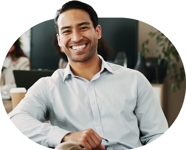 A smartly dressed man sits back in his chair with his arm resting on a table and smiles