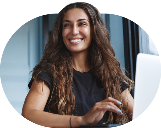 A lady working at a laptop smiling at someone close by