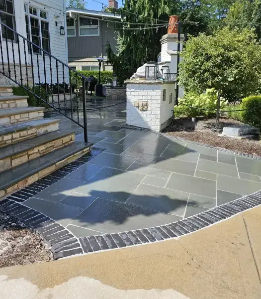 Stone patio and steps with black railing in a backyard