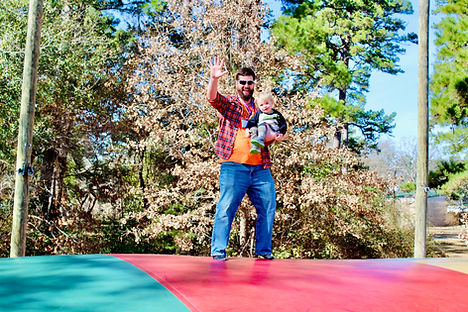 Father holding toddler and waving while standing on the jumping pillow.