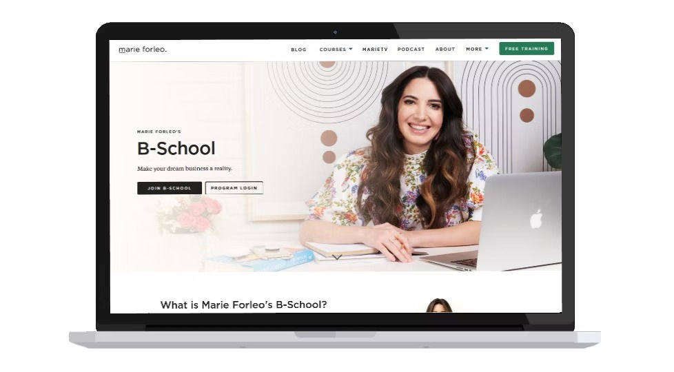 Smiling woman with long hair in colorful top, sitting at a desk with a laptop on a webpage promoting "B-School." Text: "Join B-School".