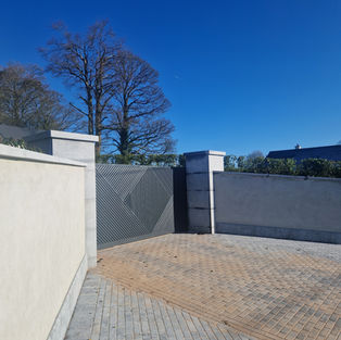 Stone wall and gate with gravel driveway under a clear blue sky. OConnell Stone.
