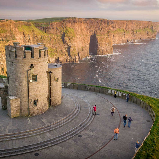 Cliffs of Moher with a stone tower, ocean, and people enjoying the view.