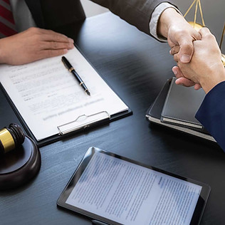 Two people shaking hands near a gavel and paperwork Greg Nolan Solicitors.