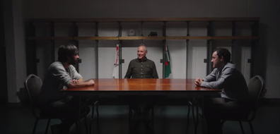Three men at table, flags in background, discussing in formal setting, Corporate Lighting.