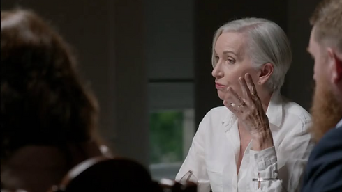 Woman with white hair talking, hand on face, discussing at the table.