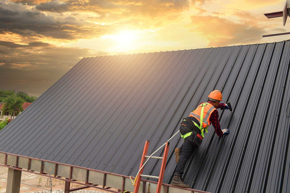 Roofer working on a dark gray roof with safety harness and ladder.
