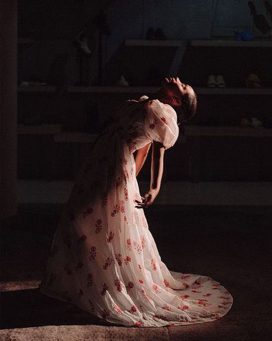 Woman in white dress with red flowers posing in dramatic lighting.