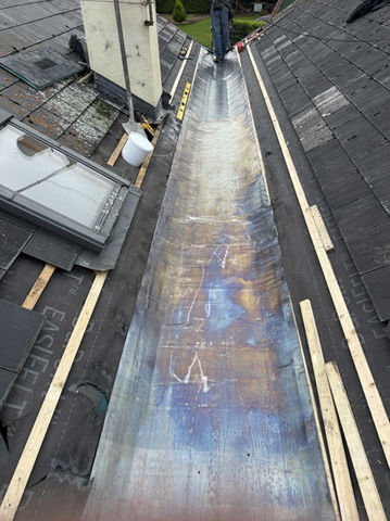 Roofers working on a long, metallic roof valley, visible construction materials in place.