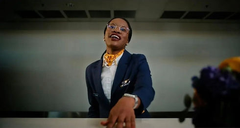 Smiling woman in uniform at desk, yellow scarf. Eoghan Hand Lighting.