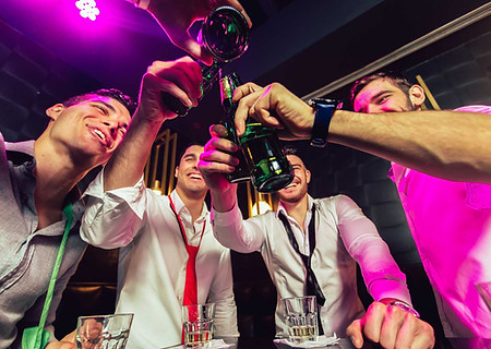 Men toasting with beer bottles in a bar, celebrating together, smiling.