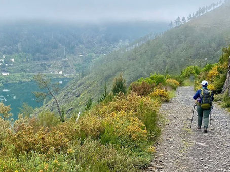 Uma pessoa caminhando em uma trilha, de um lado uma montanha, do outro um penhasco com um rio esmeralda abaixo