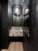 Finished powder room with a marble sink, brushed brass fixtures, an organic-shaped mirror, and dark plaster walls