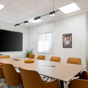 חדר ישיבות מרווח עם שולחן מרכזי וכיסאות כתומים, טלוויזיה על הקיר