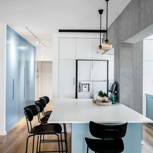 מטבח מודרני תכלת עם אי ישיבה עץ וכיסאות שחורים, פתוח לסלון מואר.