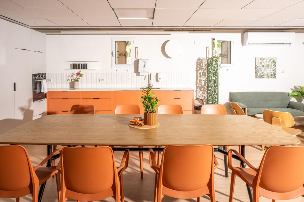 שולחן עץ גדול עם כיסאות כתומים ונגרות מאחור