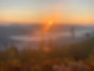 The sun is rising over the mountains. A valley below is shrouded in fog. The tips of trees punctuate the imagine.