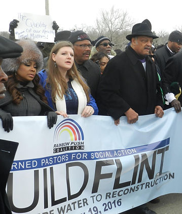 Religious leaders lead a march holding a banner saying: Rainbow Push Coalition, Rebuild Flint