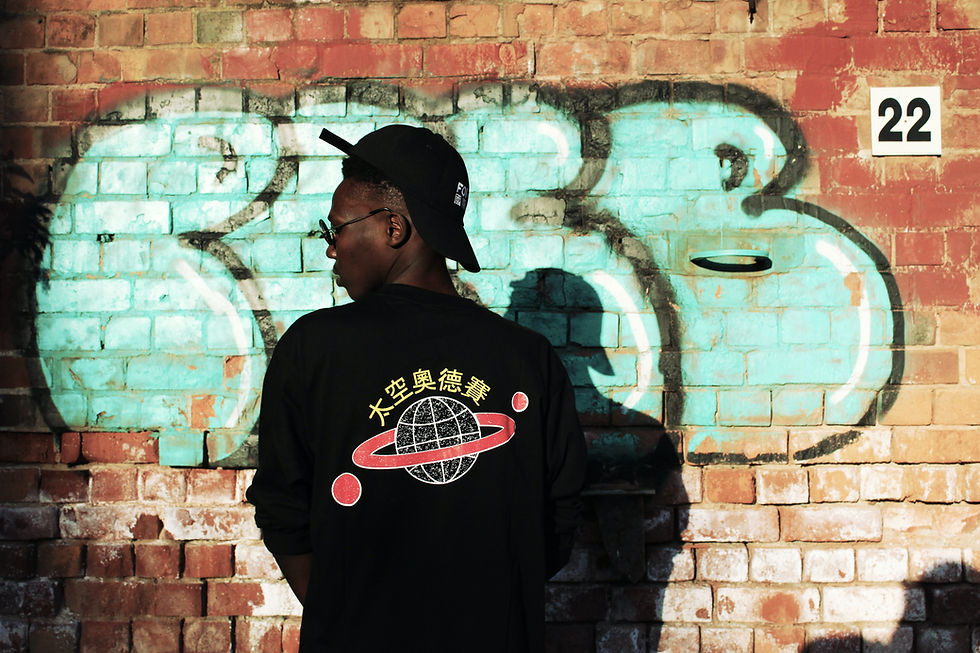 A young man stands with his back to the camera in front of a graffiti wall. - urban hip hop streetwear