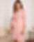 Pregnant woman in a pink robe smiles, holding her baby bump indoors