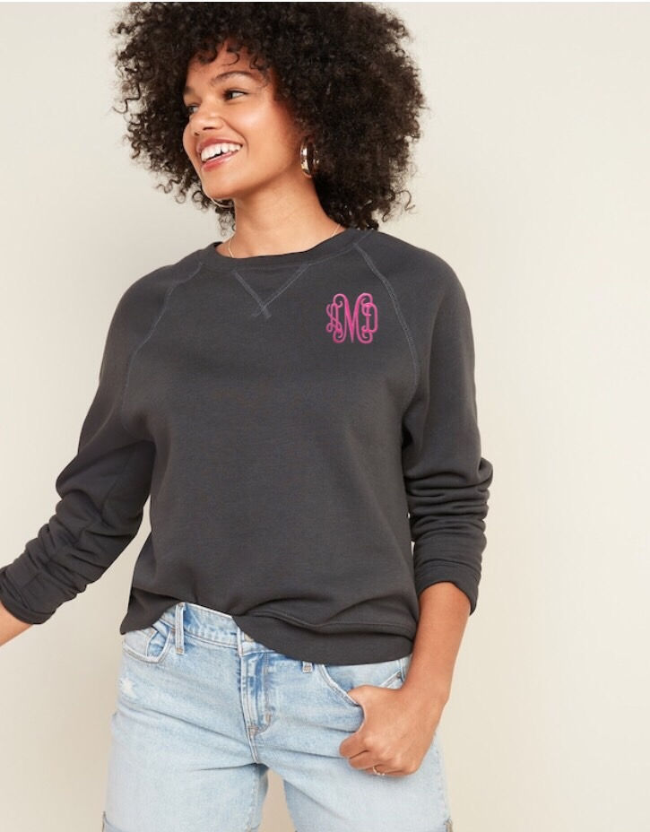 Miniatura: Smiling woman wearing dark gray sweatshirt with a pink embroidered design and text.