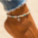 Ankle with a starfish charm and seashell anklet, beach background, close-up shot.