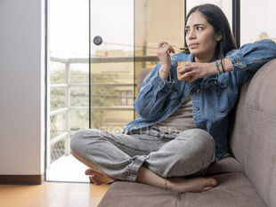 Spanish woman sitting on a couch reflecting and struggling to move on from a past relationship