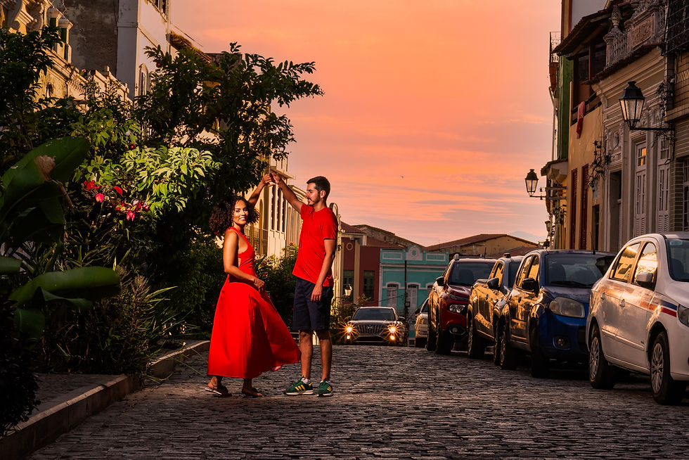 Ariana e Heleno dançando no meio da rua e ao fundo está um céu com a tonalidade do por-do-sol