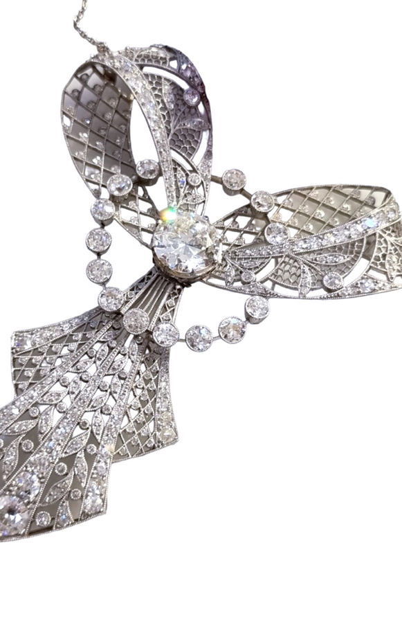 the jewelry on the bottom of the necklace is covered in diamonds with the center stone being the largest and the entire pendant is shaped like a bow with two hanging prongs and a large circle of diamonds around the center of the bow.