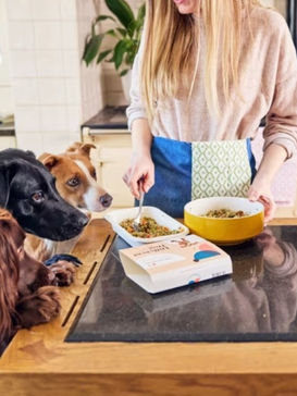 woman dishing up fresh dog food to hungry dogs