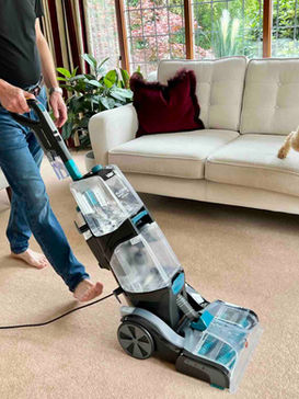 Man using a VAX carpet cleaner with dog and sofa in background