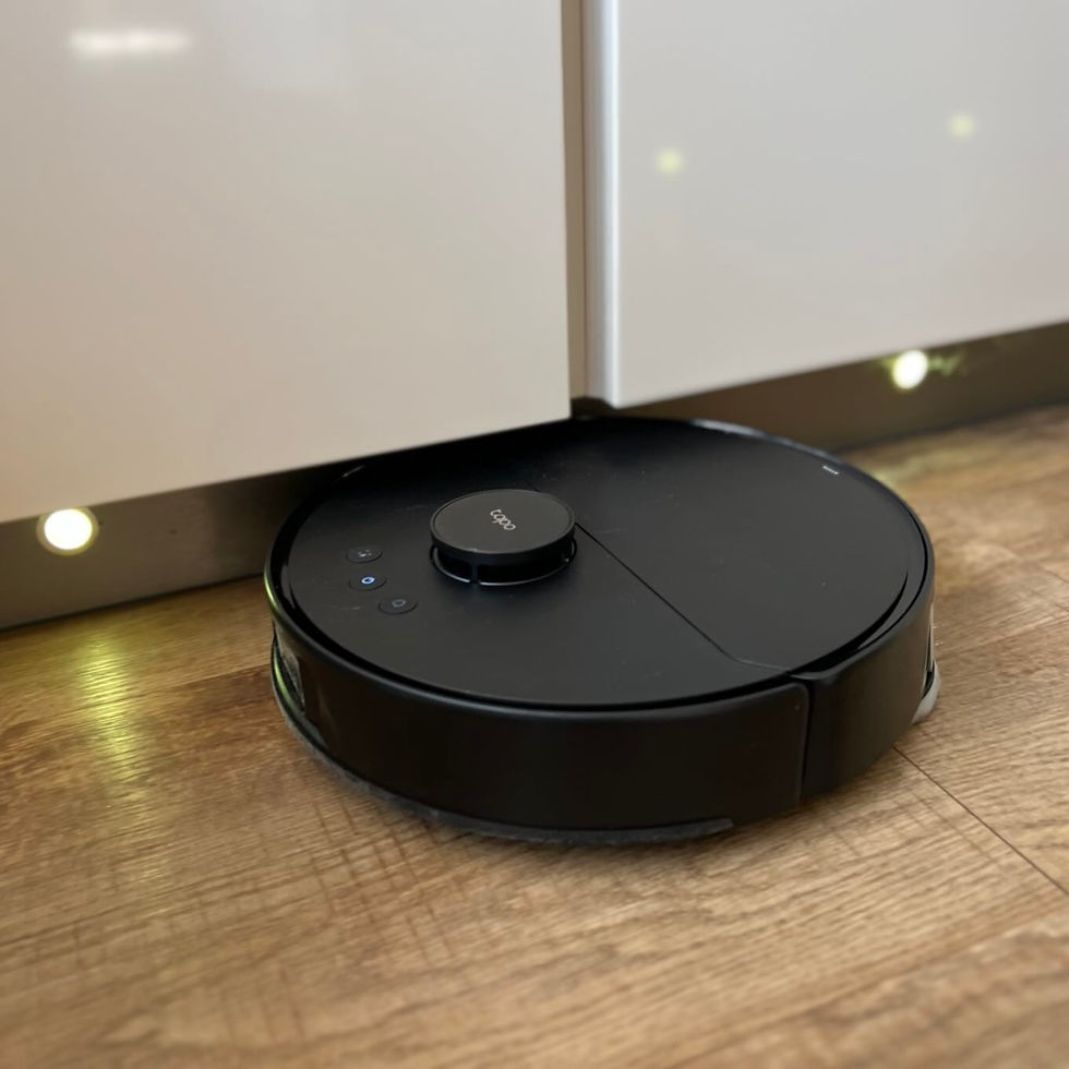 Black robot vacuum with lit buttons sits on a wood floor under white kitchen cabinets.