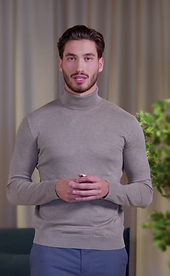 Young man in a gray turtleneck presenting confidently in a modern indoor setting, with soft lighting and a casual-professiona