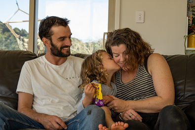 A kid kisses his mom on the cheek while sitting between his parents