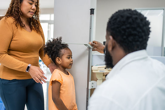Young Black girl getting height measured by doctor at clinic.