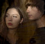 They came together like a coincidence that refused to behave like one. Two singers from different continents, both raised in towns with the same name, orbiting each other through the circuitry of the internet before colliding in the flesh at a show, as if summoned by some low, persistent hum beneath things. The band is Witch Post—a Scottish-American pairing of Dylan Fraser and Alaska Reid—and their music carries that origin story like a splinter under the skin: small, strange, impossible to ignore.

The name itself is not decorative. A witch post, in 17th-century English folklore, was carved to keep something out—to ward off what might slip down the chimney when the night loosened its grip. Witch Post, the band, invert that instinct. Their songs invite the presence in. They set a place for it at the table. They pour it a drink.

By the time they arrived at *Butterfly*—their 2026 EP released via Partisan Records—they had already mapped out a duality: *Beast* and *Butterfly*, winter and thaw, animal and apparition. Their work leans into these mirrored states, treating the everyday as something thin-skinned, ready to split open and show its teeth.

And then there is “Worry Angel,” a song that does not so much begin as it seeps in.

Released in February 2026 as a preview of *Butterfly*, and later positioned as its second track, “Worry Angel” is built from nervous rituals and private superstitions—the quiet compulsions that accumulate in the corners of a life. It runs roughly four minutes, though it feels longer, as though time itself has been made to hesitate.

The band have described the song not in technical terms but in images that coil and tighten: a “lucky keychain you can’t go anywhere without,” a presence that wraps itself around your neck, a pixie that will not leave you alone, a sense of being watched that may or may not be real.

It is, in other words, anxiety given folklore.

The lyrics move through small domestic acts—checking locks, avoiding cracks in the pavement, flicking switches for luck—until they begin to feel like incantations. The narrator insists, almost plaintively, “I’ve done everything right / so why is everything wrong?” before turning outward, addressing the unseen companion: “Why do you worry, angel?”

There is no answer. There never is.

Musically, the track draws from the lineage that hovers behind Witch Post’s work: a blend of alt-rock abrasion and dreamlike vocal interplay. Fraser’s voice carries urgency, a kind of strained confession, while Reid’s arrives like a second weather system—cooler, more diffuse—until the two begin to braid together. The effect is neither harmony nor conflict but something more ambiguous, as though two interior monologues have been forced to share the same mouth.

This doubleness is central to Witch Post. Their songs often feel like conversations between selves: believer and skeptic, body and ghost, the one who locks the door and the one who wonders if it matters. “Worry Angel” sharpens that tension into something almost tactile. The “angel” is not divine; it is intrusive, needling, parasitic. A comfort object that becomes a curse.

And yet the song resists collapsing into despair. There is a peculiar tenderness in the refrain, a reaching toward something that might steady the hand. “Give me something I can hold,” the voice pleads, not with grandeur but with exhaustion.

That exhaustion is where Witch Post live. Not in the spectacle of suffering, but in its repetition—the way it loops, returns, reshapes itself into new symbols. Pixies, crows, angels, talismans: the band’s imagery draws from folklore, but it is repurposed for a modern interior life, where the hauntings are as likely to be psychological as supernatural.

“Worry Angel” sits at the centre of *Butterfly* like a small, dark jewel. Around it are songs of shifting landscapes—county fairs, fawns, restless travel—but here the focus narrows to the private theatre of the mind.

What Witch Post understand, perhaps instinctively, is that the old language of myth still functions, even now. Not as belief, exactly, but as metaphor with teeth. Anxiety becomes a creature. Loneliness becomes an omen. A passing thought becomes a winged thing that will not leave.

And so the song ends as it began: circling the question, never resolving it.

Why do you worry, angel?

The line hangs there, unanswered, like a door left slightly open in a house that has already decided it is haunted.

