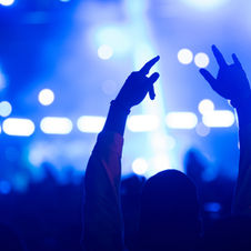 A mesmerizing concert scene with a silhouette of a fan enthusiastically raising their hands towards the vibrant stage lights, capturing the electric atmosphere.