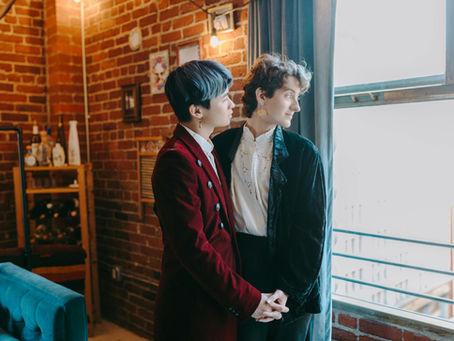 LGBTQ+ couple looks out of the window from inside a brick room.
