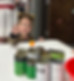 There is a little girl dressed in leopard print with cat ears. She is standing behind a white table. The table is almost at her shoulders. She is throwing an orange ping ball. There's a group of painted, halloween colored cans and the orange ball is above one of the cans.