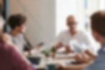 A group of people in business attire sit around a table talking.