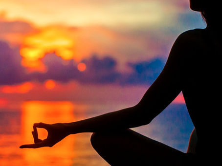 Silhouette of a person meditating by the sea at sunset