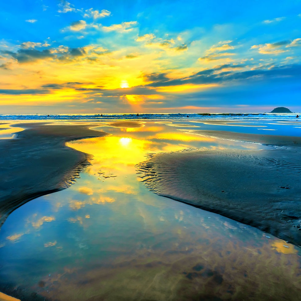 Sunset over a beach with vibrant orange and blue skies reflecting on wet sand. The serene mood is enhanced by gentle waves in the background.