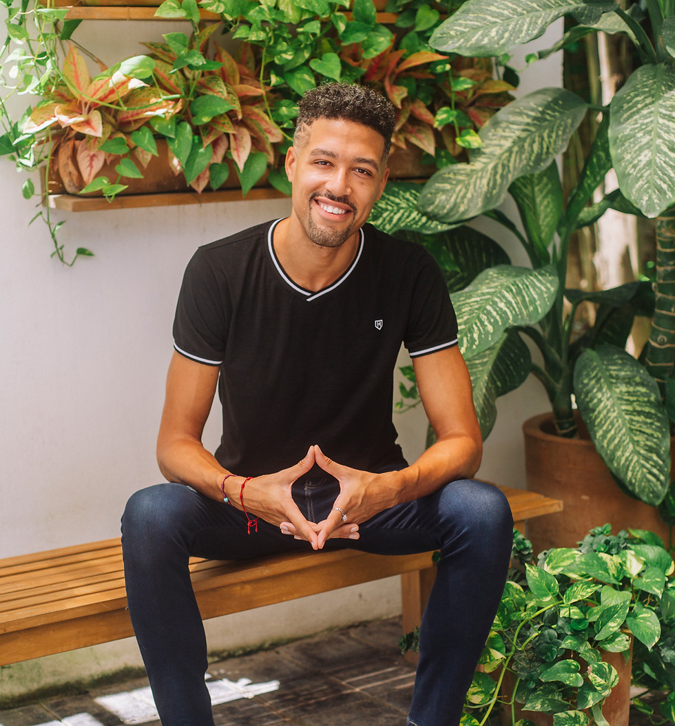 Portrait of Dil sitting on a wooden bench surrounded by lush green plants