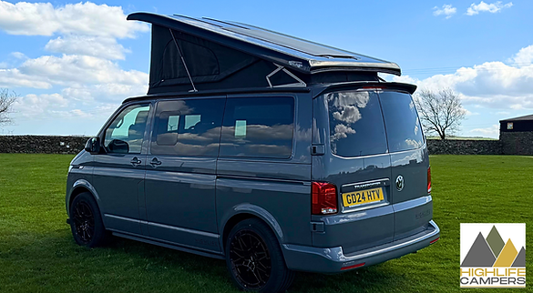 Rear view of grey VW T6.1 Highline Explorer with pop-top extended, dry stone wall in the background