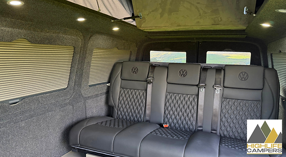 Rock-and-roll bed and rear lounge inside VW T6.1 Highline campervan with carpet-lined walls and ambient LED lighting