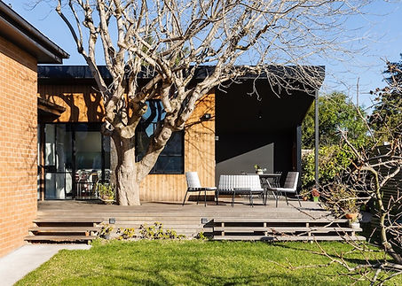 How do you turn an orange brick 1950’s ugly duckling into a stunning contemporary home with good access to light and connection to garden? This house in the Eastern mid-suburbs of Melbourne only had a few good things going for it: it had 4 bedrooms and 2 bathrooms, many of the rooms had good north-facing access, and the original part of the house had characterful steel-framed corner windows, albeit in pretty terrible condition. On the downside, the house was dark, cold, a rabbit-warren and the only view from the house to the back garden was looking straight into the shed. In addition, there was a large deciduous Box Elder tree right outside the back door which needed to be retained. 

The dark south side of the house was reassigned to service functions only, and a new courtyard. To get around small bedrooms without any storage, a number of walk-in-robes were built. New doors between living spaces open up to give more direct circulation, light penetration and views to the outside. The real highlight, however, is the tree which is now the centre around which the house revolves and provides a green shady aspect in summer and sun-filled living spaces in winter. 

The small kitchen extension turns the house around to face to the north-facing rear garden across a large deck and outdoor eating area located around the tree. Given the Mediterranean background of one of the owners outdoor entertaining is a huge focus and the deck and outdoor dining area provide this beautifully. They have recently extended this even further with a built in woodfired pizza oven & outdoor lounge area. Aperol spritz anyone?