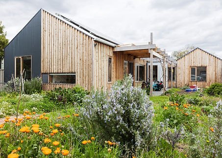 The owners of this new house in Melbourne's inner north prioritized sustainability and sought to maximize productive garden space. They were also completely committed to using bicycles for transport and, with two young children, had a variety of bikes including electric cargo bikes that they wanted stored hanging inside the front hallway. The early design meetings were consumed by discussions of how the bicycle storage was going to work and this generated the roof form and height at the front of the house. It also gave the house the nickname in our office The Bike Shed House.
The brief also included three bedrooms, accommodation for visiting grandparents, separate living and dining spaces, a craft room, a study, accessibility, durability, and minimal acoustic reverberation. All this, with a budget of $700K.

Town Planning regulations often mandate a minimum front setback – in this case one third of the site. Generally front gardens serve a purely psychological function as a transition from the public to the private zone. Whilst conforming with regulations, this house design challenges the convention, comprising multiple wings oriented for passive solar gain while creating two sizable garden areas: a main north-facing garden that extends to the street and a productive rear garden. The owners love the side garden as it gives them a really good connection to the neighbourhood and they have quickly become part of the local community. The study at the front further enhances safety by offering street visibility for children playing and pedestrians at night.

Gable roof forms harmonize with the established streetscape of single-story houses. The back bedroom wing incorporates a concealed cutaway in the gable roof, allowing high-level north-facing glazing for natural light and warmth. 

The kitchen/dining area is the heart of the home, connecting to decks in both garden areas and featuring detailed joinery.

Lots of exposed internal thermal mass was used to store winter heat from the sun but this creates sound reverberation so, unusually for a residential project, the ceilings of the house are lined with acoustic panels. 

Another unique feature is the rabbit run, as pet rabbits inhabit the laundry and access the kitchen via a cat door, with a custom terracotta rabbit-hole leading to an external run.

Cost-saving measures guided design choices including minimizing internal corridors, compact bathrooms with basic fittings, and economical external cladding materials like Cypress Macrocarpa board and batten. The craft room serves as a multi-functional space with daybed and fold-down Murphy bed for guests. Accessibility features are concentrated in the front two wings, reducing expenses. Unlined reverse blockwork walls minimised linings and painting and the pasterboard ceiling lining was unpainted except for the shadowline gaps between panels and where lights and other ceiling mounted fittings were located. 

In summary, The Bike Shed House creatively blends sustainability, bike-friendliness, and community engagement while meeting diverse living needs and budget constraints.