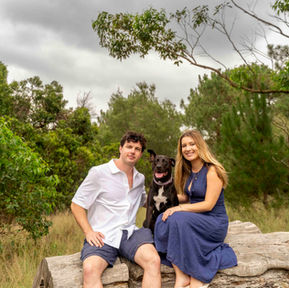 Couple sitting on a tree trunk with their dog during an outdoor photoshoot at Centennial Park, Sydney, enjoying natural light and relaxed moments.