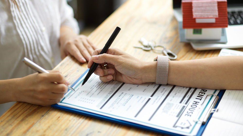 A stock photo of a woman signing a document to rent a house