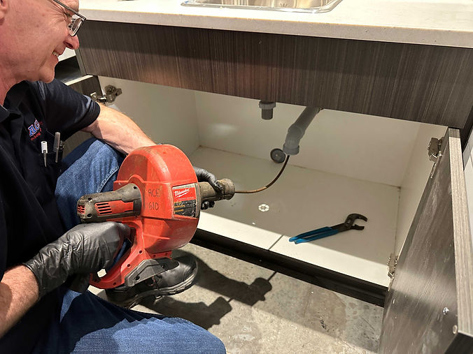 An ACE Plumbing and Heating employee cleans a drain using an auger